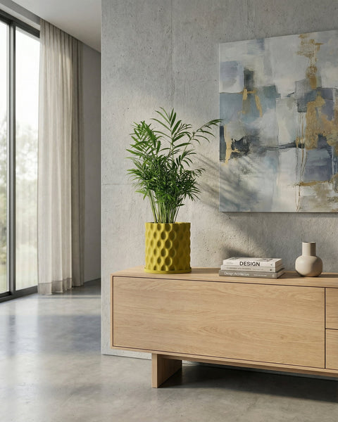 A green plant in a yellow planter pot sits on a wooden cabinet. The pot has a textured, geometric design.
