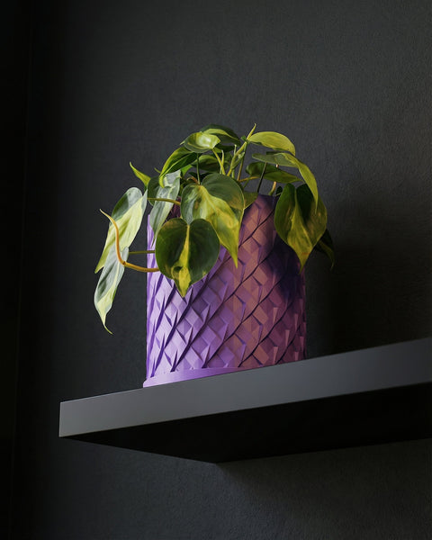 A purple planter pot with a green plant inside sits on a concrete floor in front of a window.