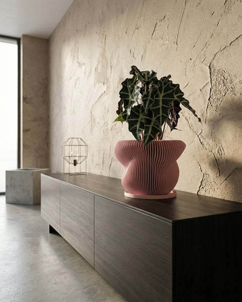 A pink planter pot with a spider plant sits on a dark wooden cabinet against a mustard-colored wall.