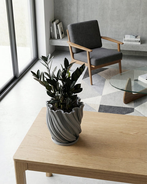A gray planter pot with a green ivy plant sits on a wooden shelf against a rust-colored wall.