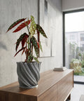 A gray, textured planter pot with a peace lily sits on a wooden console table in a modern entryway with a round mirror.