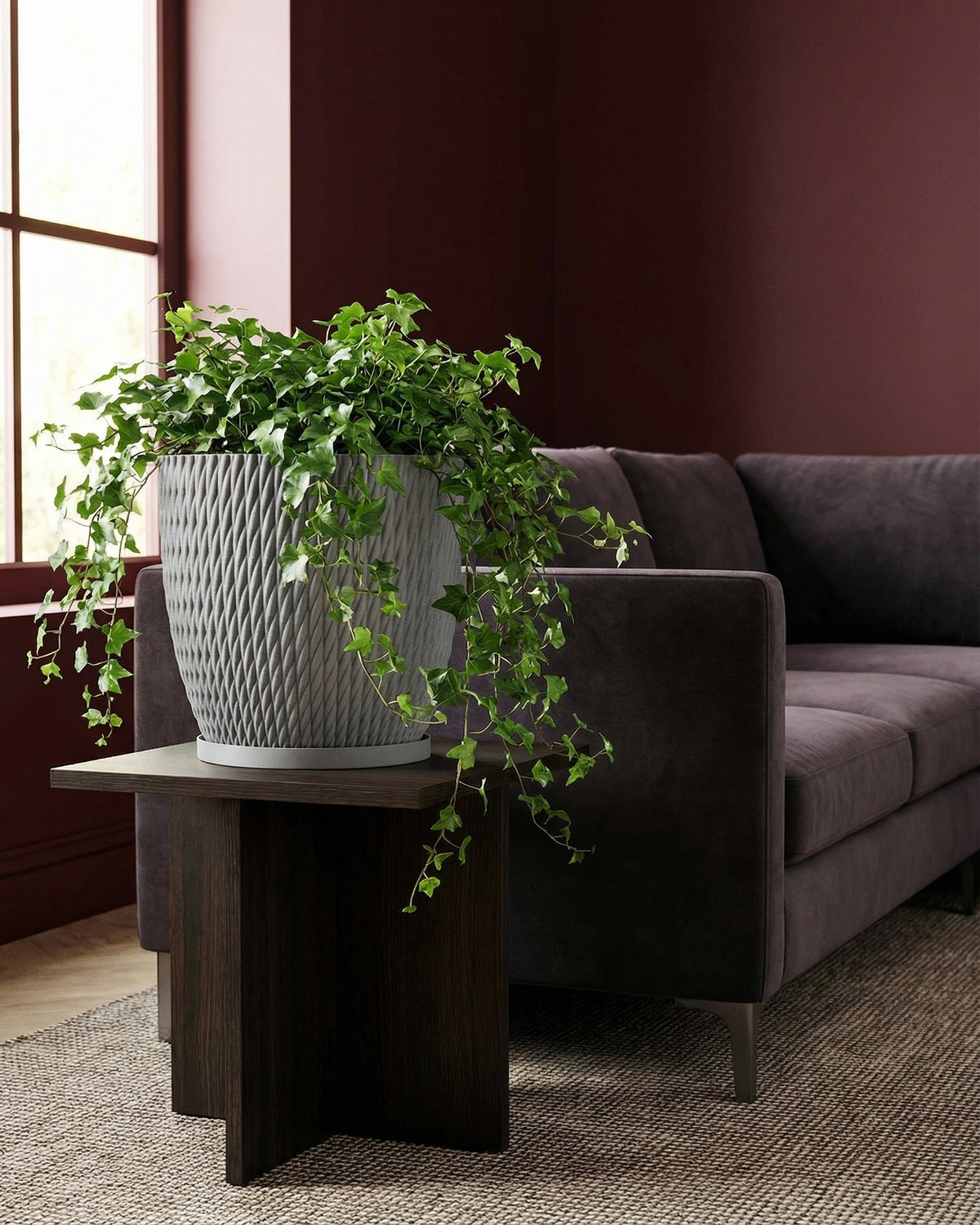 A gray planter pot with a green ivy plant sits on a dark wood table next to a brown couch.