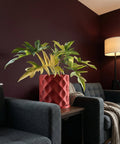 A red planter pot with a plant in it sits on a table between two gray chairs. A lamp is in the background.