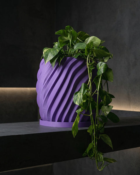 A purple planter pot with a plant in it sits on a gray shelf. The pot has a swirling design.