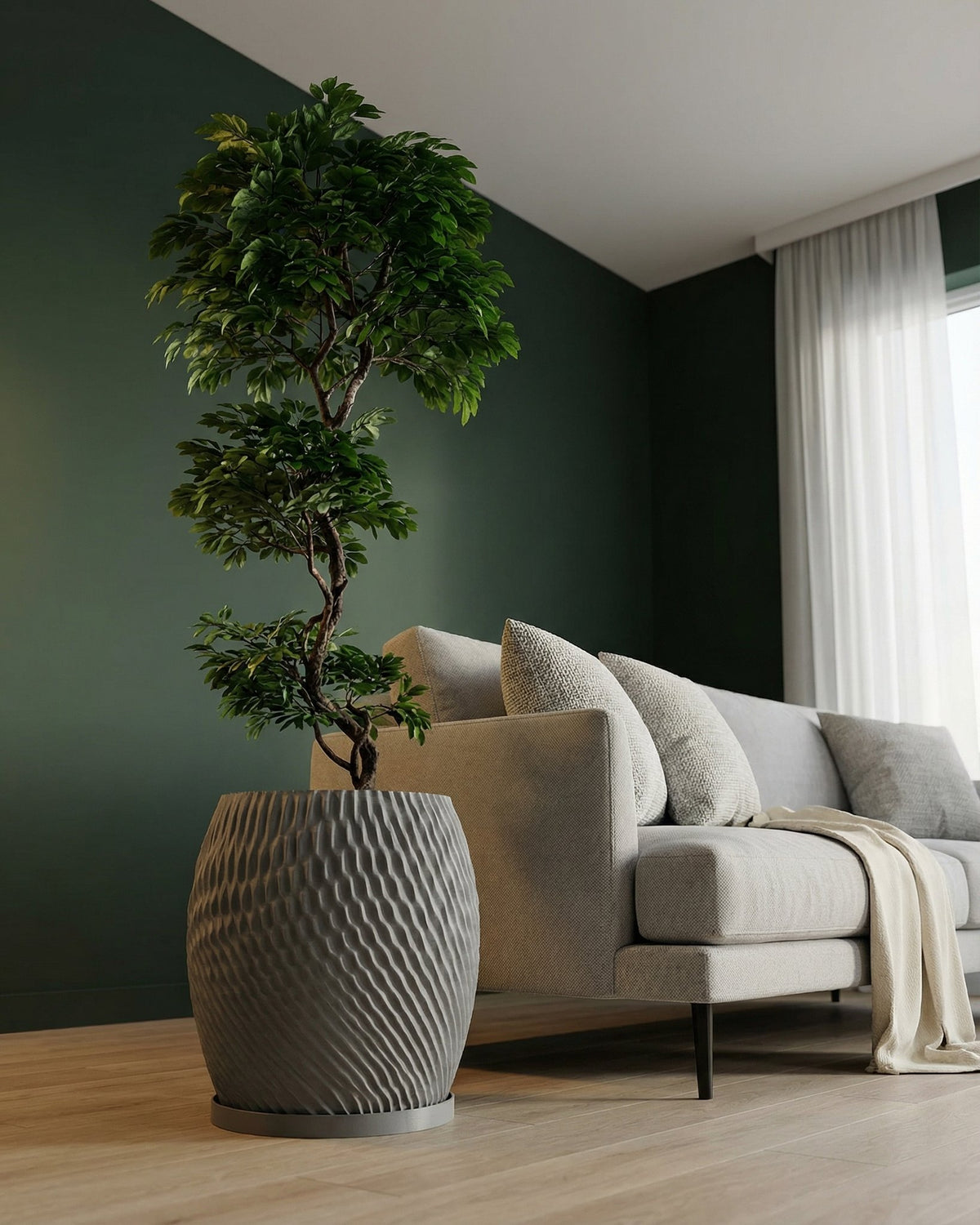 A gray planter pot with a textured, swirling design sits next to a light gray sofa with pillows and a throw blanket. A green plant is in the pot.