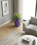 A spider plant in a purple planter pot sits on a dark wood table next to a gray sofa.