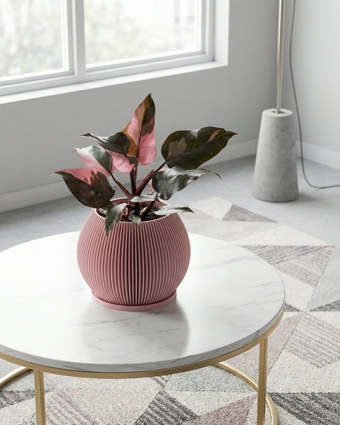 A pink planter pot with a plant sits on a white marble table with gold legs. The pot has a ribbed texture.