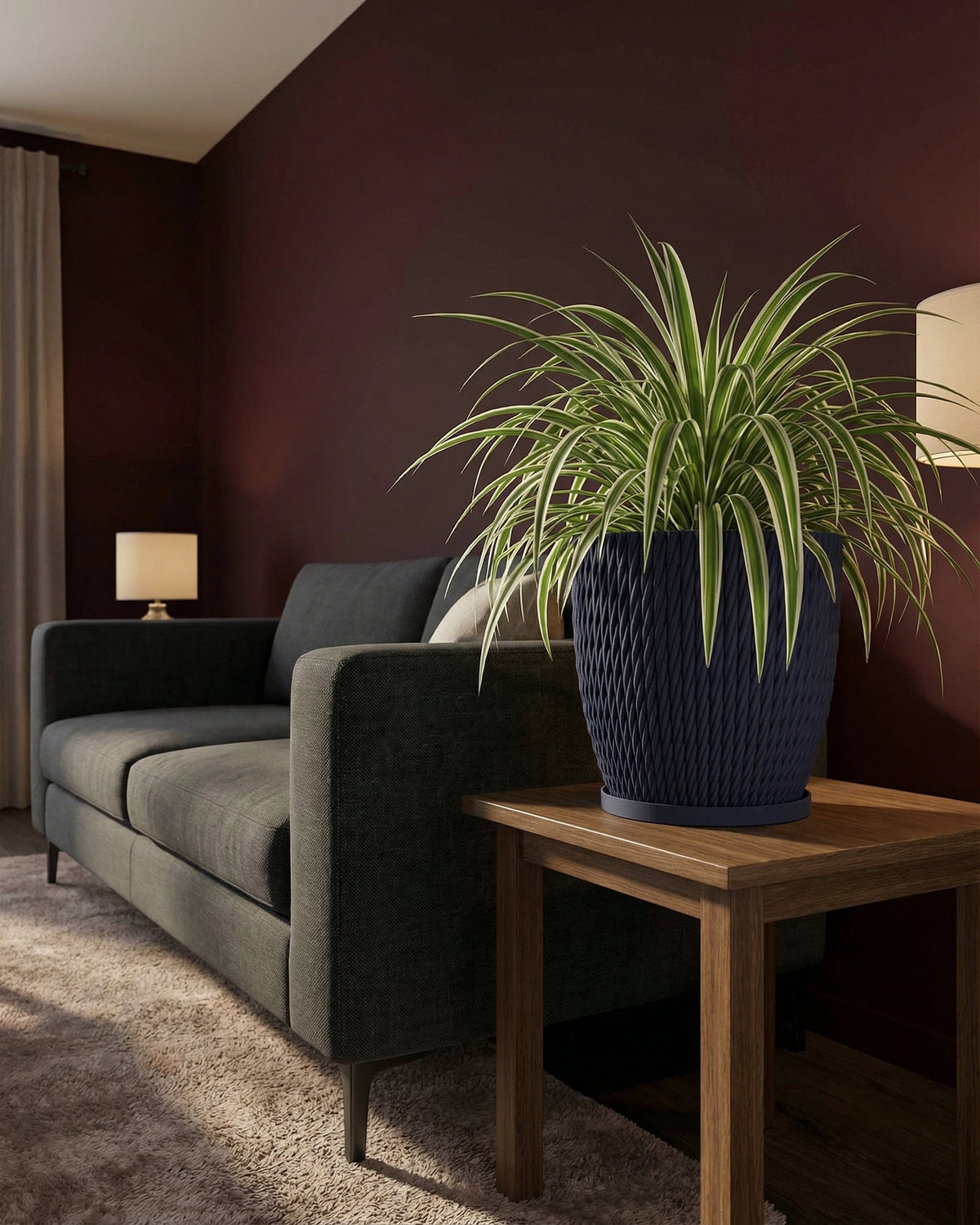 A spider plant in a navy blue woven planter pot sits on a wooden side table next to a gray sofa in a living room.