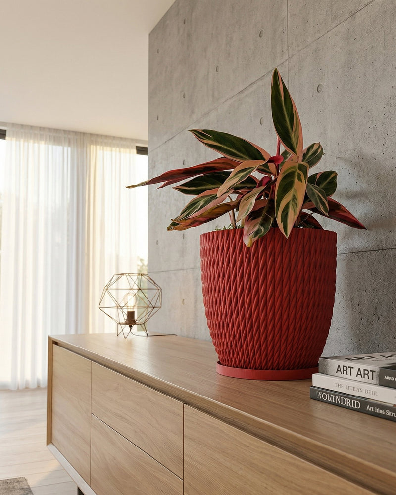 A red planter pot with a plant sits on a wooden cabinet next to books and a lamp.