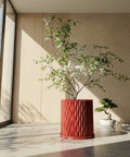 A red planter pot with a plant sits on a dark wooden bench in a room with dark green walls and a round gold mirror.