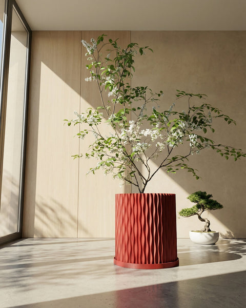 A red planter pot with a plant sits on a dark wooden bench in a room with dark green walls and a round gold mirror.