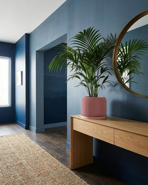A pink planter pot with a rubber plant on a wooden windowsill next to a window with a curtain.