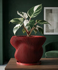 A red, round, slatted planter pot filled with a lush green ivy plant sits on a dark wood shelf next to books and a gold sculpture.