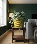 A yellow planter pot with a plant sits on a brown table next to a gray couch in a living room.