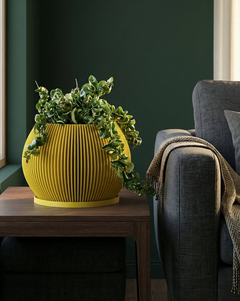 A yellow planter pot with a green plant sits on a wooden table next to a gray couch with a throw blanket.