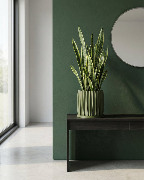A green planter pot with a plant next to a gray chair in a room with green walls.