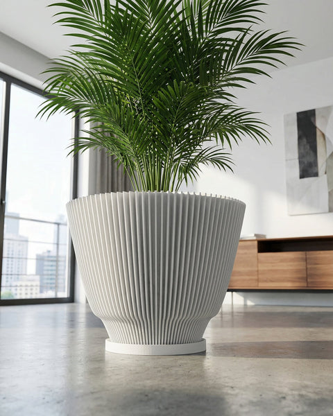 A large, white, fluted planter pot with a green plant inside sits on a gray concrete floor in a modern room. The pot has a unique, vertically ribbed design. A window with a city view is visible in the background.