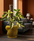 A vibrant yellow planter pot with a green plant inside sits in a modern living room with large windows and a sleek design.