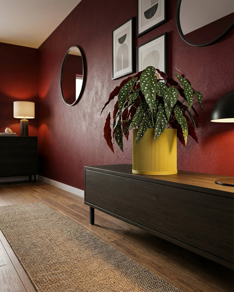 A yellow planter pot with a polka dot plant sits on a dark wood cabinet in a room with red walls.