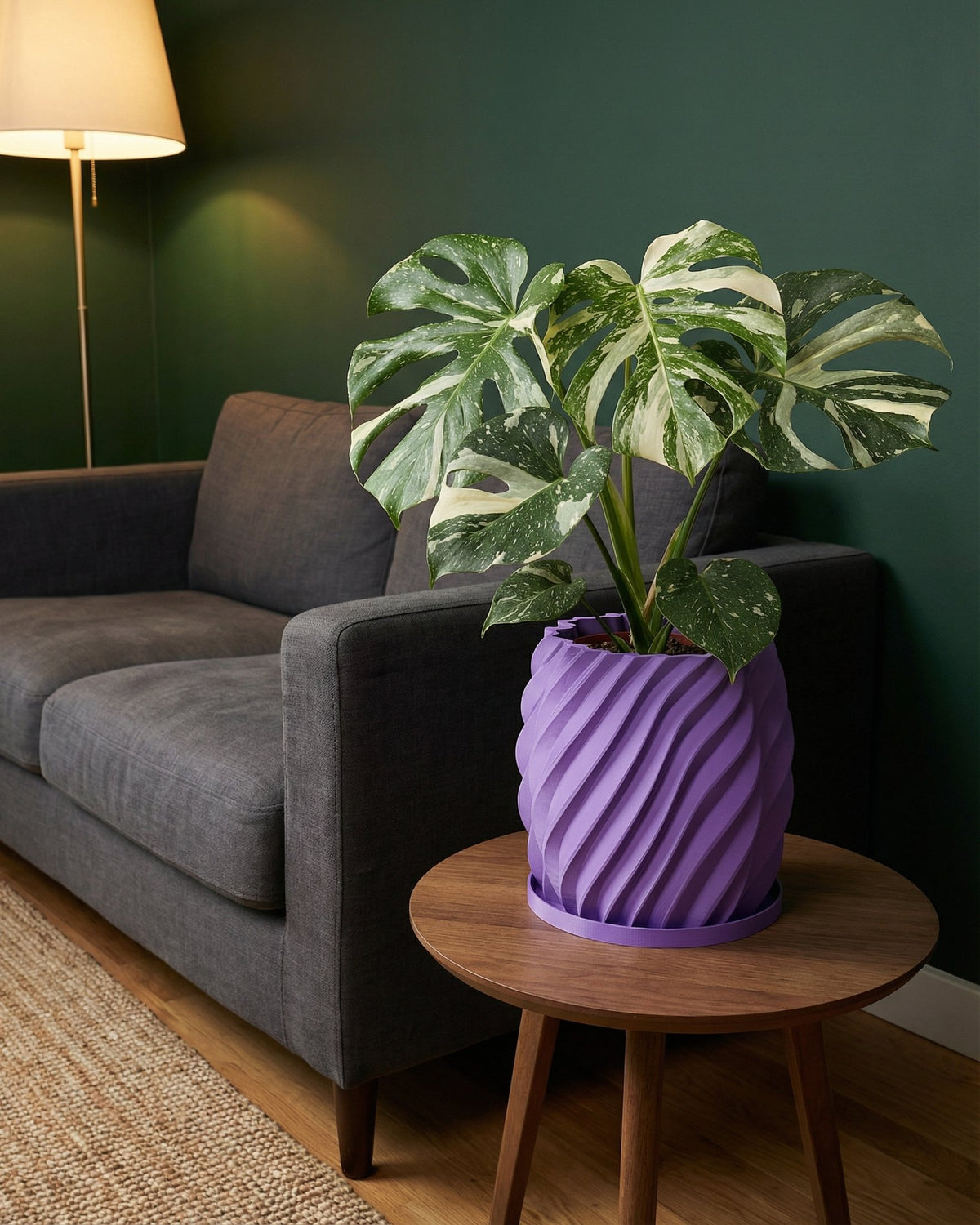 A Monstera plant in a purple, twisted planter pot sits on a wooden side table next to a gray couch.