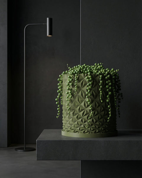 A green string of pearls plant in a geometric planter pot sits on a dark gray surface against a dark background.
