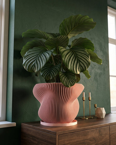 A pink planter pot with a string of pearls plant sits on a wooden table next to a gray couch in a room with dark green walls.