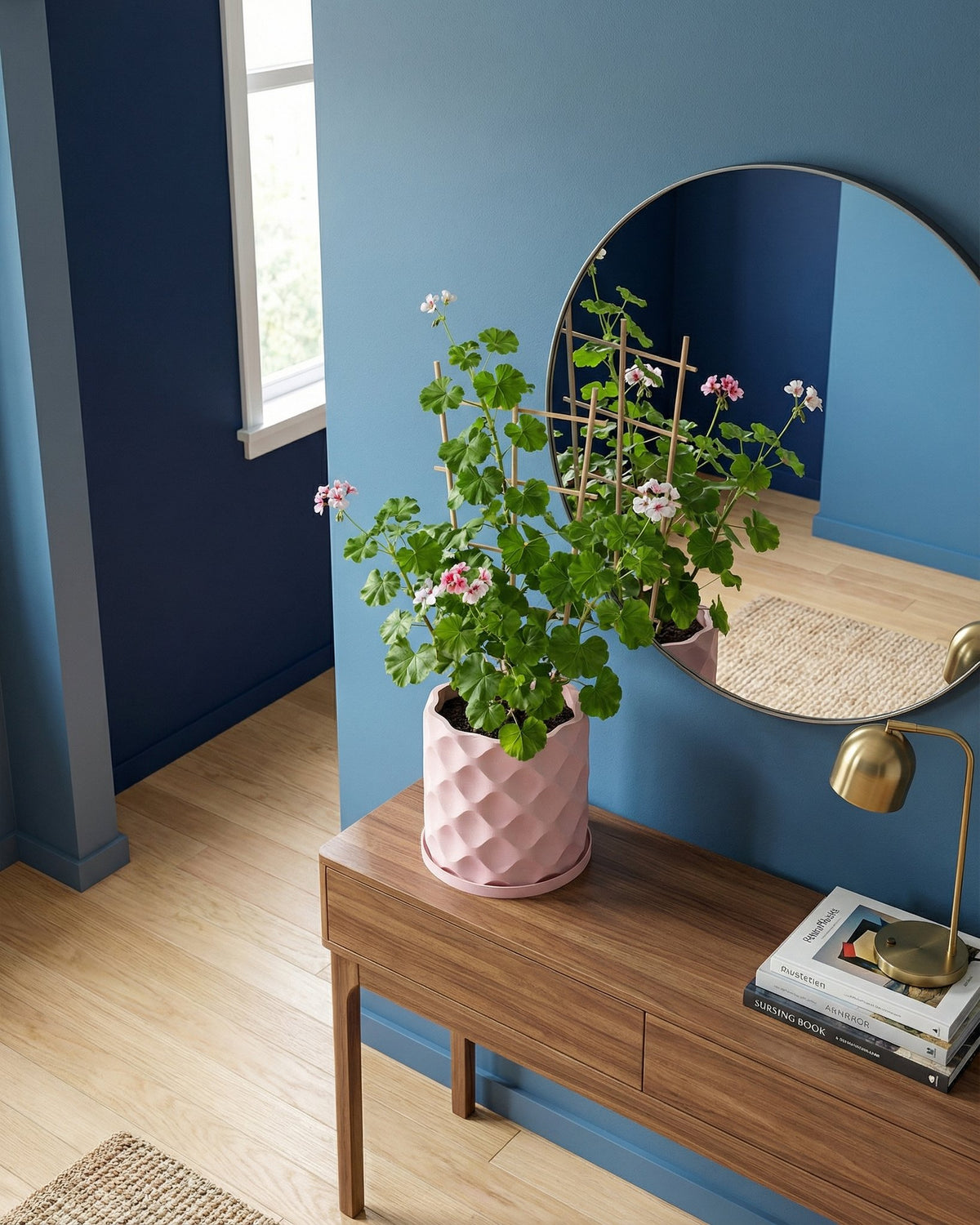 A pink planter pot with a plant on a wooden table, next to a round mirror and a lamp. The pot has a geometric pattern.