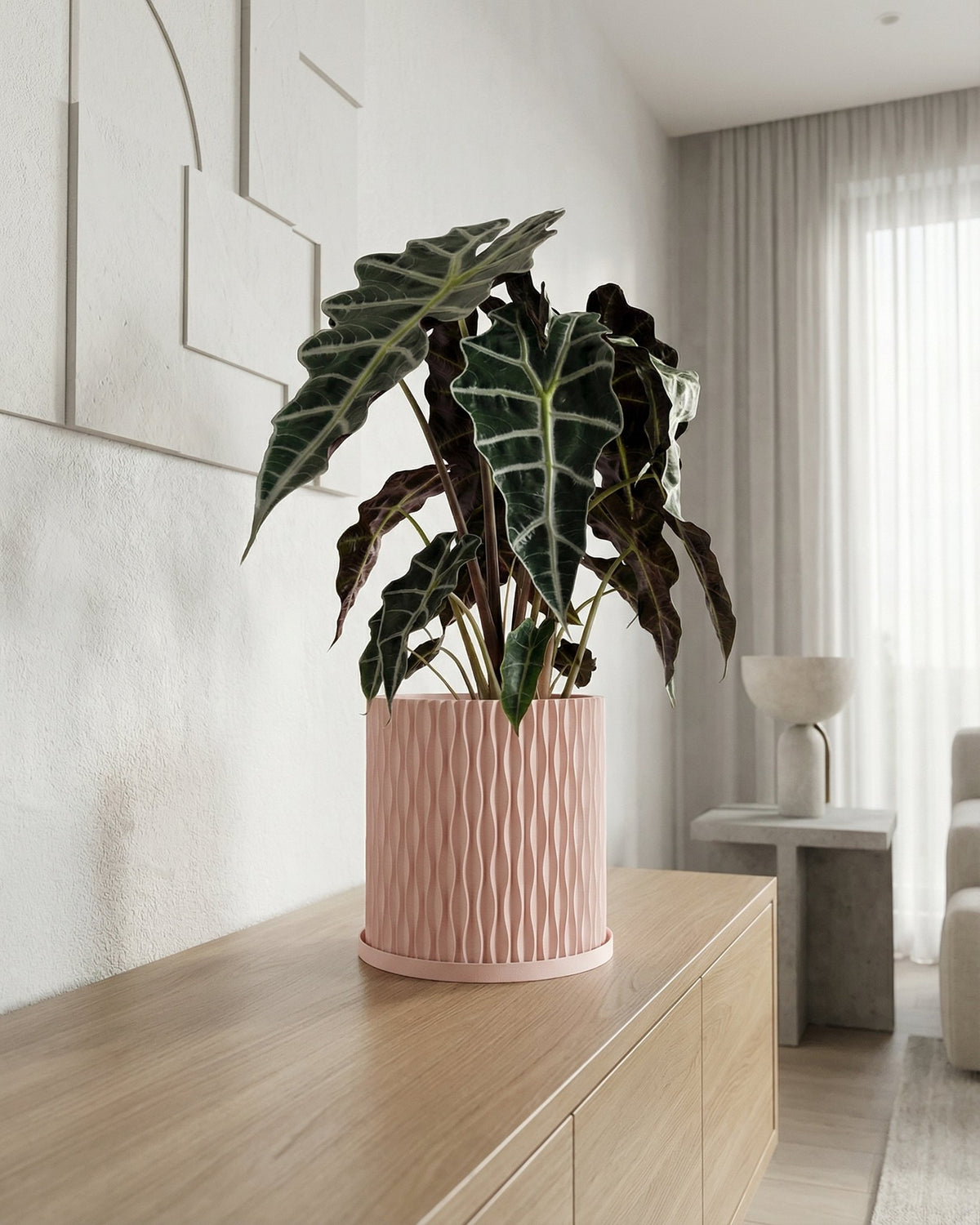 A pink planter pot with a green plant sits on a wooden table next to books and a gold lamp.