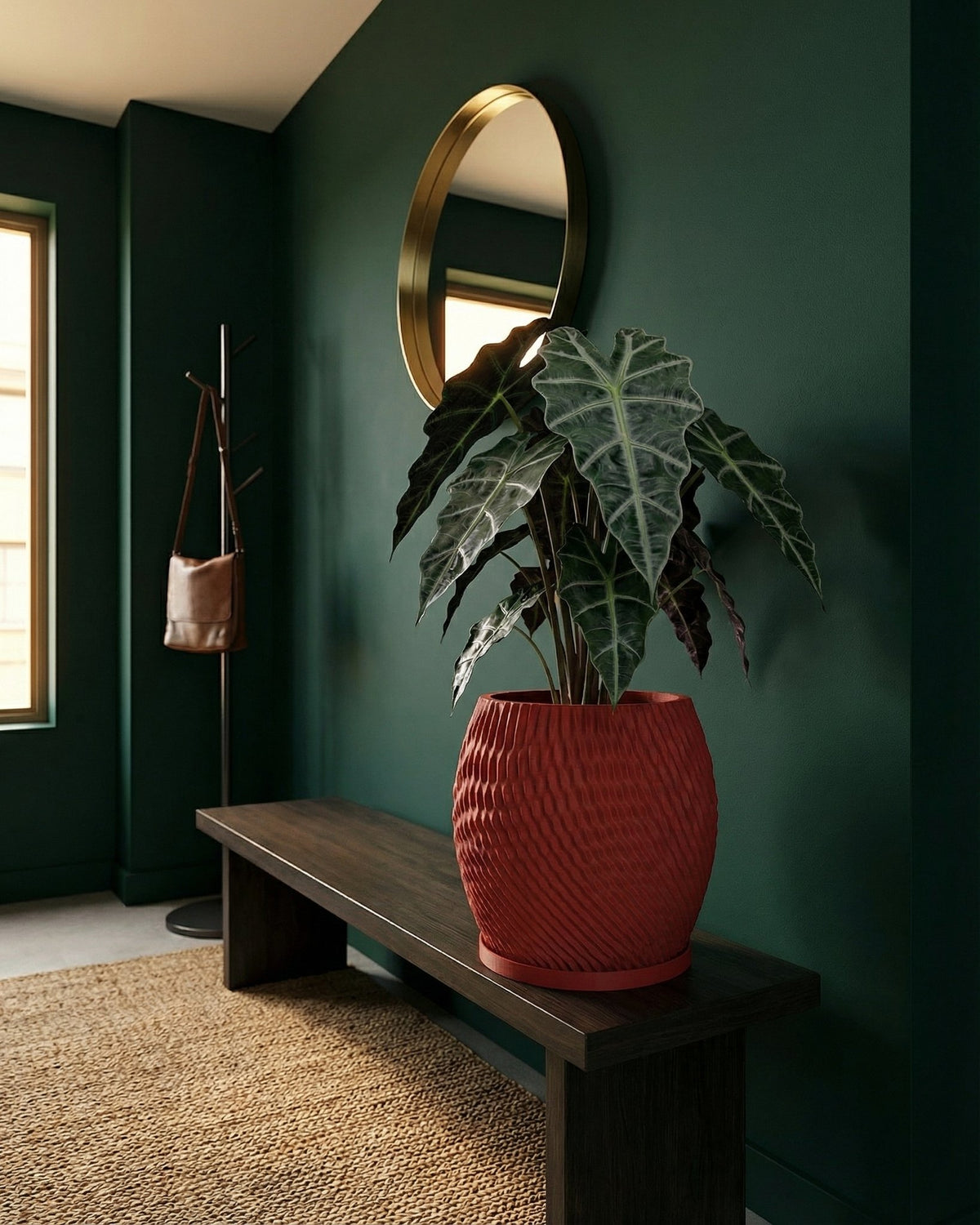 A red planter pot with a plant sits on a dark wooden bench in a room with dark green walls and a round gold mirror.