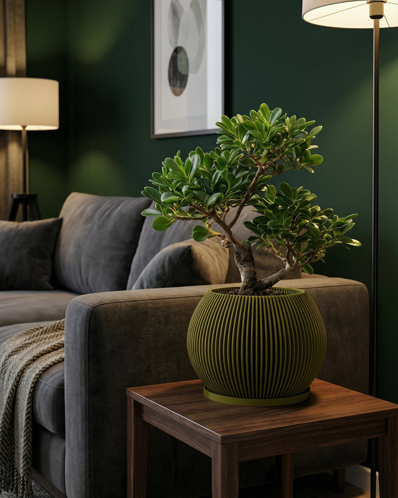 A green planter pot with a bonsai tree sits on a wooden table next to a gray couch in a living room.