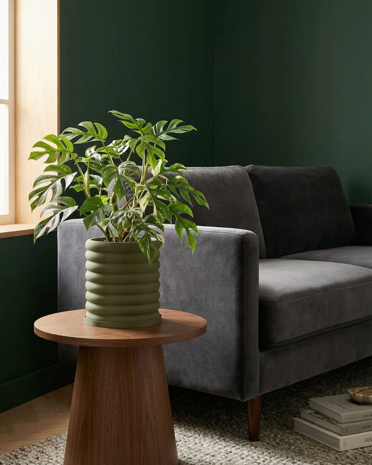 A green planter pot with a plant on a wooden table next to a gray couch.