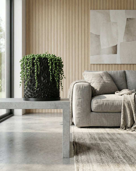 A black planter pot with a string of pearls plant sits on a concrete table in a modern living room.