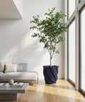 A ZZ plant in a textured, dark blue planter sits on a wooden shelf against an orange wall with a window.