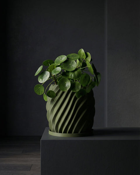 A green Pilea peperomioides plant in a matching green planter pot with a spiral design, sitting on a dark gray surface.