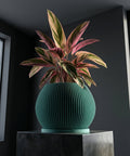 A green planter pot with a plant inside, sitting on a gray pedestal. The pot is round and has vertical lines.