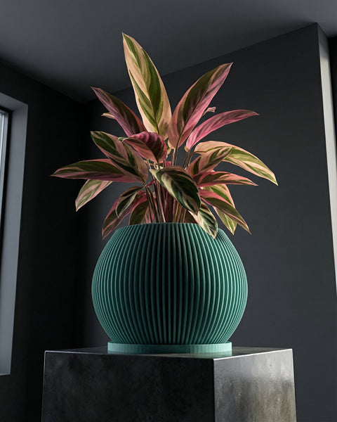 A green planter pot with a plant inside, sitting on a gray pedestal. The pot is round and has vertical lines.