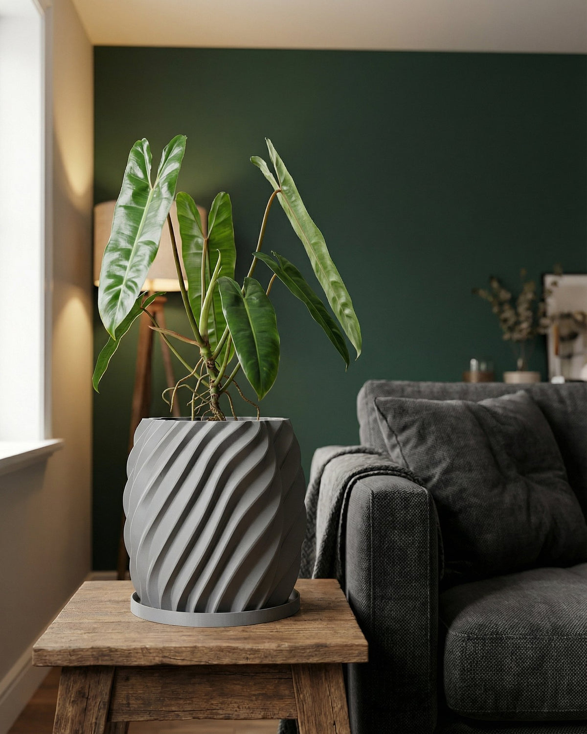 A gray planter pot with a green plant sits on a wooden table next to a gray couch. The planter pot has a unique, swirling design.