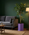 A living room scene with a gray sofa, a wooden table, a floor lamp, and a vibrant purple planter pot holding a lush green plant.