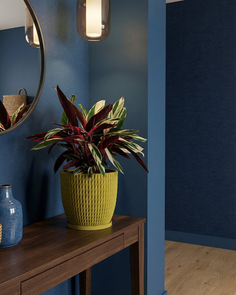 A vibrant plant in a textured, yellow planter pot sits atop a dark wooden table, adding a pop of color to the blue-toned room.