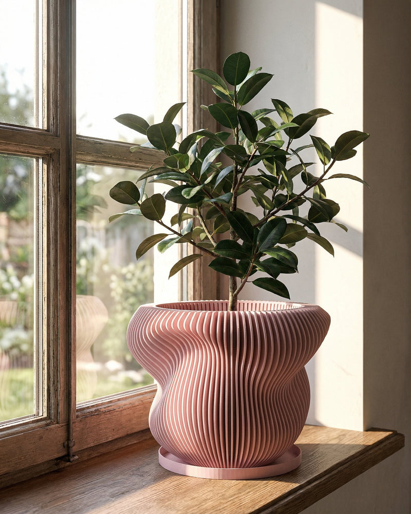 A small green tree in a pink, vertically striped planter pot sits on a dark gray surface against a dark gray wall.