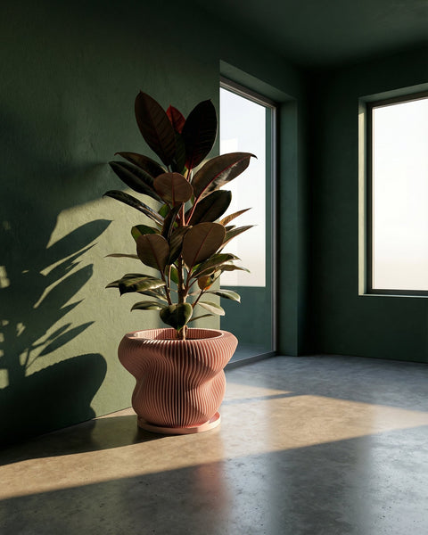 A pink planter pot with a plant sits on a white marble table with gold legs. The pot has a ribbed texture.