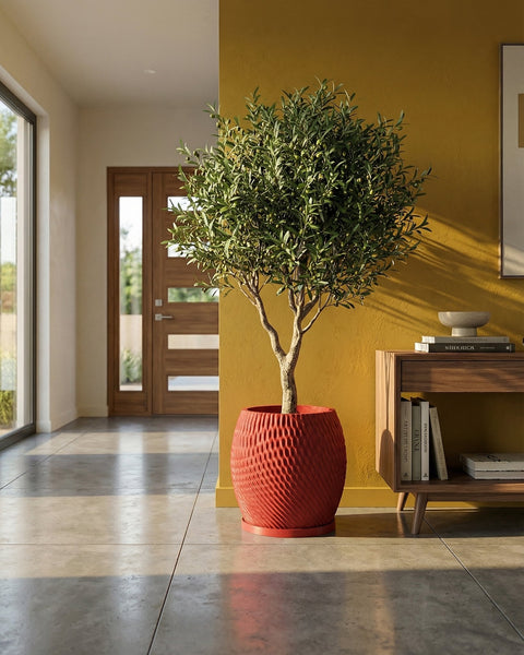 A red planter pot with a textured surface sits on a gray floor, holding a small tree with green leaves. A wooden cabinet is nearby.