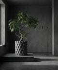 A gray planter pot with a plant inside sits on a gray platform in a gray room with a gray lamp.