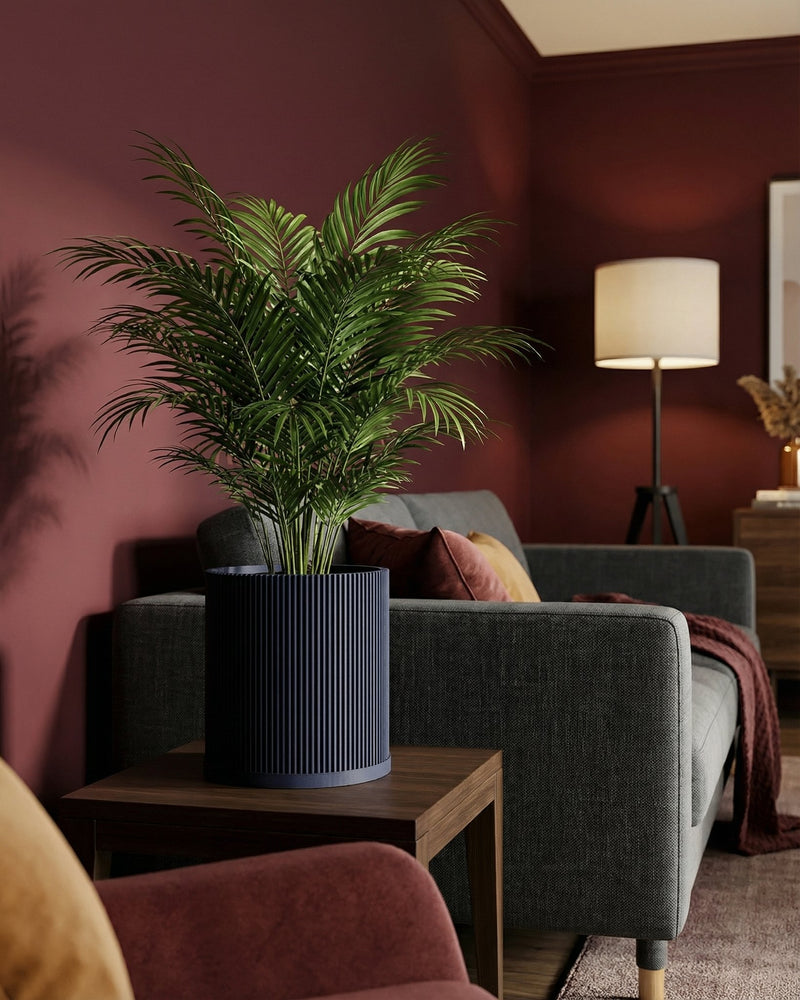 A vibrant green plant sits in a dark blue, vertically ribbed planter pot, placed on a wooden side table next to a gray sofa.
