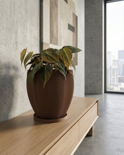 A brown textured planter pot with a green plant next to a gray couch on a wooden floor.