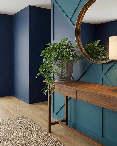 A gray planter pot with a green plant on a wooden table, with a round mirror in the background.