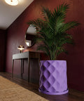 A purple planter pot with a geometric design sits on a dark wood floor next to a plant.