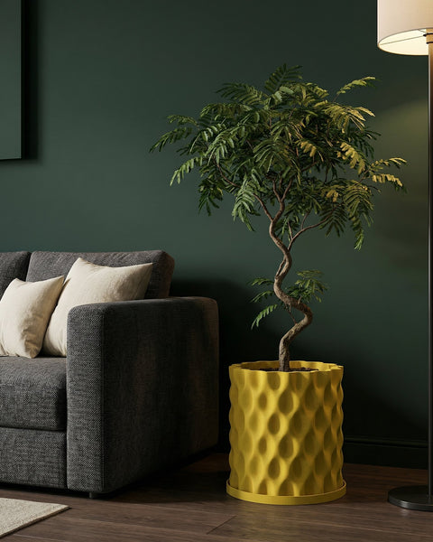 A yellow planter pot with a textured design sits next to a gray sofa and a floor lamp, holding a small tree with green leaves.