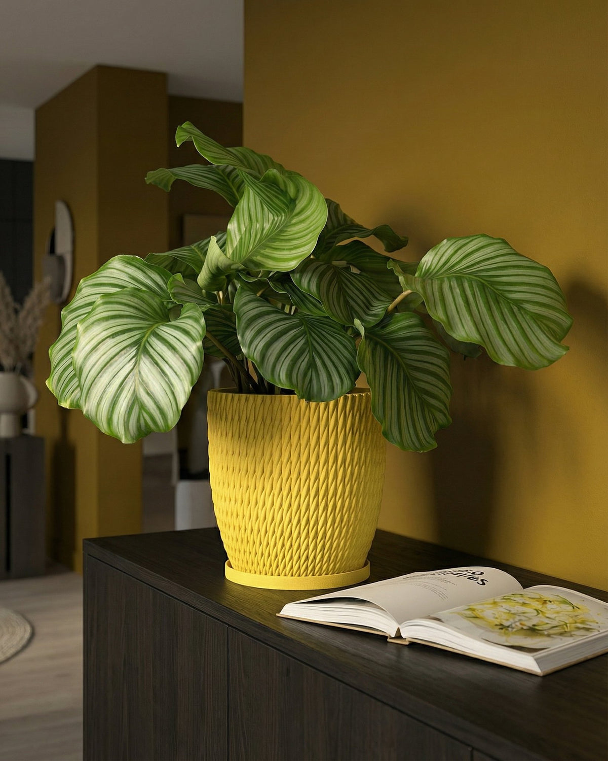 A yellow planter pot with a plant on top of a dark brown cabinet with a book on it.