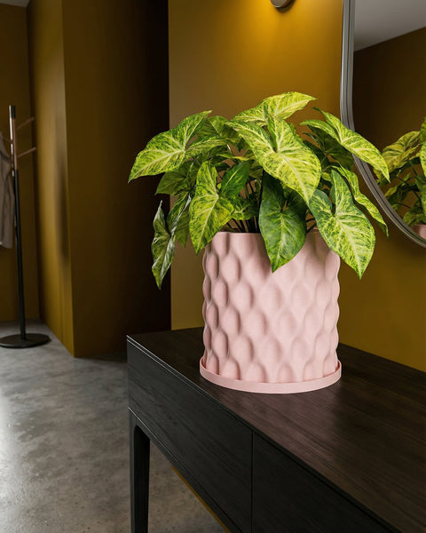 A pink planter pot with a green plant sits on a dark brown table in a room with yellow walls and a mirror.